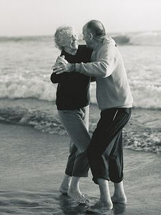 an older couple hugging on the beach by the water