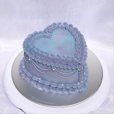 a blue heart shaped cake sitting on top of a white platter with silver trim