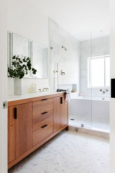 a bathroom with a sink, mirror and bathtub next to a plant in a vase