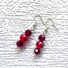 These charming drop earrings each have a central 10mm (0.4in) shiny round bright red glass bead surrounded by two 8mm (0.3in) ruby red faceted acrylic beads.   The beads dangle from silver-plated ear wires with small silicone stoppers to hold them securely in the ear.  The total length of the earrings is 4.5cm (1.8in).   Earrings will be sent to you in a lovely 3.2 x 2in (8 x 5cm) silver gift box.  The price includes UK postage. International postage is reduced accordingly.  Gifts can be sent directly to the recipient. Just choose the gift option at check out. Bead Drop Earrings, Handmade Dangle Earrings, Ribbon Decorations, Silver Gift Box, Earrings Handmade Dangle, Beaded Drop Earrings, Beaded Dangles, Red Glass, Acrylic Beads