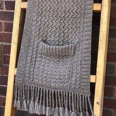 a crocheted blanket sitting on top of a wooden ladder next to a brick wall