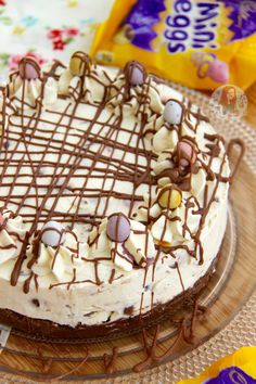 a chocolate cake with white frosting on a glass plate next to candy bar wrappers