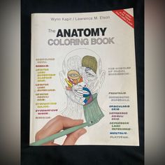 the anatomy coloring book is being held by a person's hand with a green marker