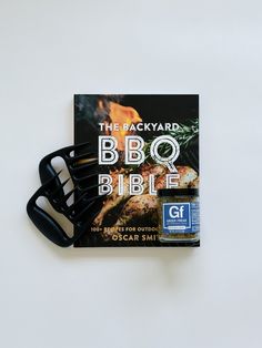 the backyard bbq bible with tongs resting on it's side next to an open grill