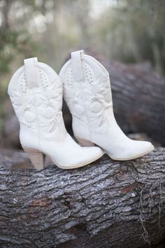 a pair of white cowboy boots sitting on top of a tree branch