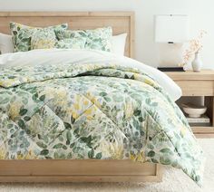 a bed with a green and yellow comforter on top of it next to a night stand