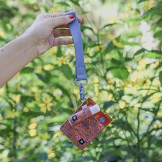 a hand holding a lanyard id badge in front of some plants