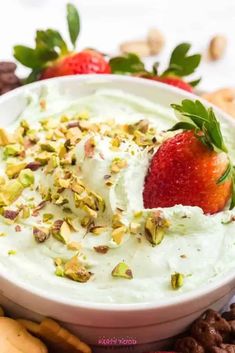 a white bowl filled with whipped cream and topped with strawberries, nuts, and pistachios