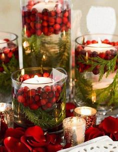 some candles are sitting in glass vases with red flowers and greenery on them