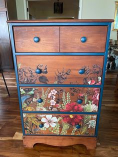 an old dresser with flowers painted on it's sides and blue trim around the drawers