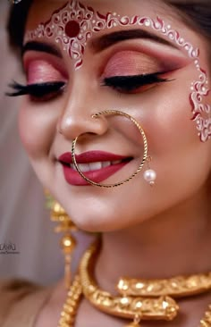 a woman with gold jewelry and makeup looks into the distance while wearing a red lip ring