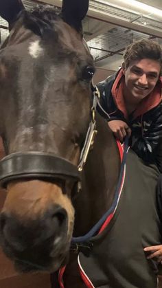 two men standing next to a brown horse in a stable with another man sitting on top of the horse