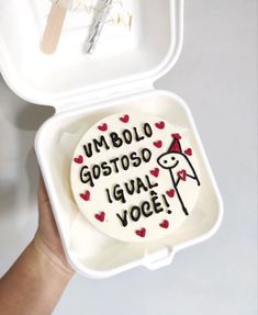 someone is holding up a small cake in a white box with writing on the inside