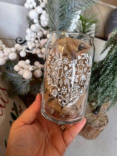 a person holding up a glass jar filled with coins and christmas tree branches in the background