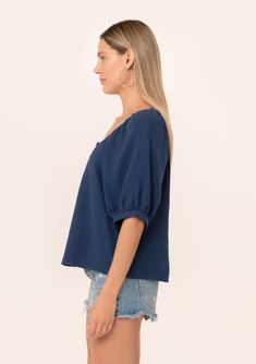 A navy blue bohemian puff sleeve blouse designed in soft cotton gauze. Cotton gauze Relaxed fit Short raglan puff sleeve Round neckline with contrast thread detail Button front Bohemian summer blouse A contrast thread detail adds a unique charm to this classic bohemian blouse. Designed in soft cotton gauze, featuring raglan puff sleeves, a flattering scooped neckline, and a button front. Model is 5'9, wearing a size S.Style: I-15055W-RJZ Blue Balloon Sleeve Blouse For Daywear, Bohemian Cotton Blouse With Square Neck, Spring Short Sleeve Cotton Gauze Tops, Spring Cotton Gauze Short Sleeve Tops, Chic Indigo Summer Blouse, Blue Blouse With Gathered Sleeves For Daywear, Swiss Dot Cotton Blouse, Cotton Swiss Dot Blouse, Indigo Blouse For Summer