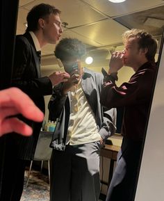 two men standing in front of a mirror with one man brushing his teeth and the other looking at his reflection