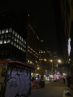 a city street at night with graffiti on the wall and buildings in the background,