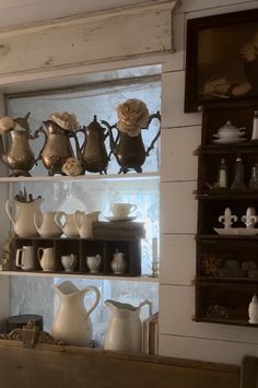 the shelves are filled with different kinds of teapots and pitchers on display in front of a window