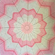 a pink and white crocheted blanket on top of a bed