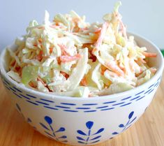 a white and blue bowl filled with coleslaw on top of a wooden table