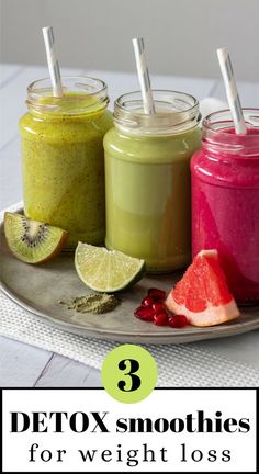 three mason jars filled with different types of smoothies on a silver plate next to sliced fruit