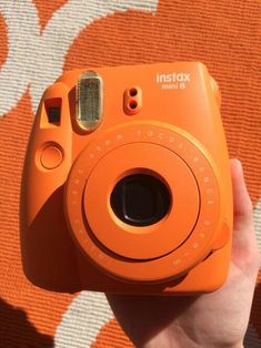 an orange instax mini 8 camera being held up