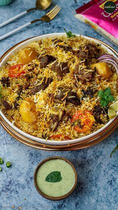 a bowl filled with rice and vegetables on top of a blue table next to silverware