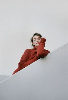 a woman in a red sweater leaning on the edge of a stair case with her hands behind her head