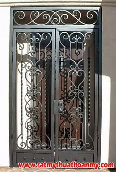 an ornate iron gate is shown in front of a stucco wall and doorway with glass doors