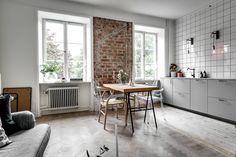 a living room filled with furniture next to a kitchen and dining table in front of a brick wall