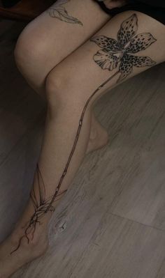 a woman sitting on the floor with her legs crossed and flowers tattooed on her leg