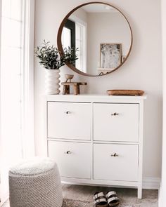 a white dresser with a round mirror above it and a pair of slippers on the floor