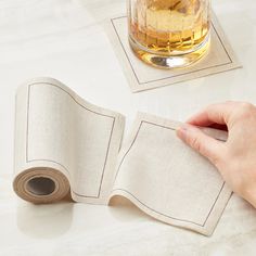 someone is holding the edge of a piece of cloth next to a glass of alcohol