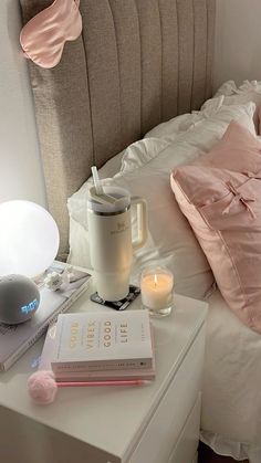 a bed with pink pillows, books and a lamp on top of the night stand