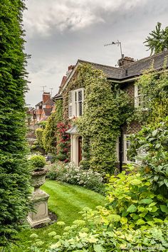 an old house covered in vines and greenery next to a garden with a grave