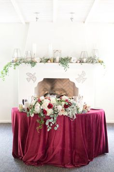 a table with flowers and candles on it in front of a fire place decorated with greenery