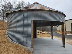 a round metal structure sitting on the side of a road next to a hill with trees