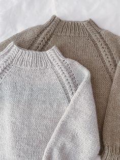 two sweaters sitting next to each other on top of a white sheet covered bed