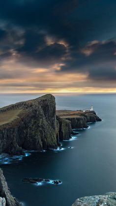 a lighthouse on top of a cliff near the ocean under a cloudy sky at sunset