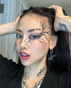 a woman with tattoos on her face and hands behind her head, wearing a black shirt