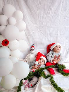 two baby dolls laying on top of a bed next to white balloons and garlands