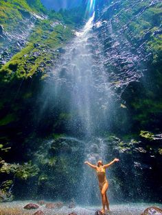 a woman standing in front of a waterfall with her arms spread out to the side