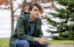 a young man sitting on the ground in front of trees