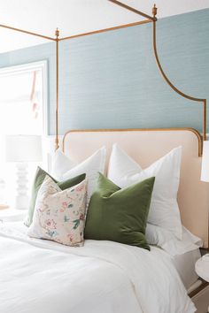 a bed with white and green pillows on top of it next to a window in a bedroom