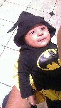 a baby dressed up in a batman costume and hat, sitting on a tiled floor