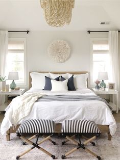 a white bedroom with black and white accessories on the bed, two nightstands, and a chandelier hanging from the ceiling