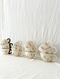 five coffee cups are lined up on a white tablecloth, with gold stars painted on them