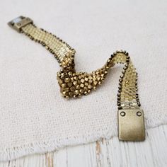 a gold and black beaded bracelet laying on top of a white cloth