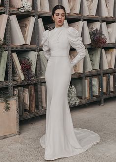 a woman in a white dress standing next to shelves full of vases and flowers