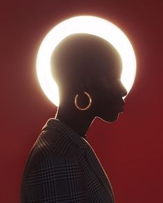 the silhouette of a woman with large earrings stands in front of a bright light circle